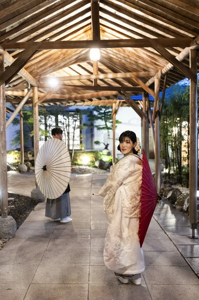 別府・神和苑の白無垢姿の新婦が番傘を持ち、新郎と二人で振り返る和装フォトウェディング